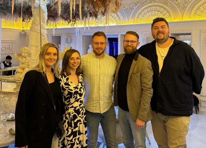 A group image in a fancy restaurant wearing business casual wear in front of a Greek statue.